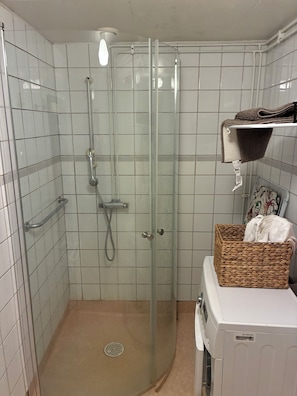 Un baño con cabina de ducha de vidrio, un perchero, una cesta y una lavadora.