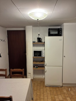 Una cocina compacta con un refrigerador blanco, un microondas y una estantería con diversos objetos.