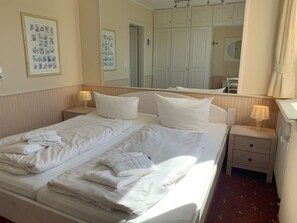 A hotel room with a bed, two bedside tables, a mirror, and a wardrobe. - 16 in the Uthlande House (Wyk auf Foehr)