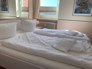 Ein ordentlich bezogenes Bett mit weißen Leinen und Kissen, eine Nachttischlampe und ein Heizkörper.
