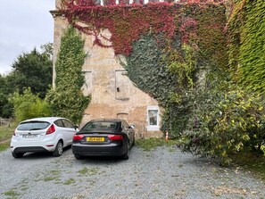 Two cars parked on a gravel path beside a building with ivy-covered walls. - Vrbo Property (Bourg)