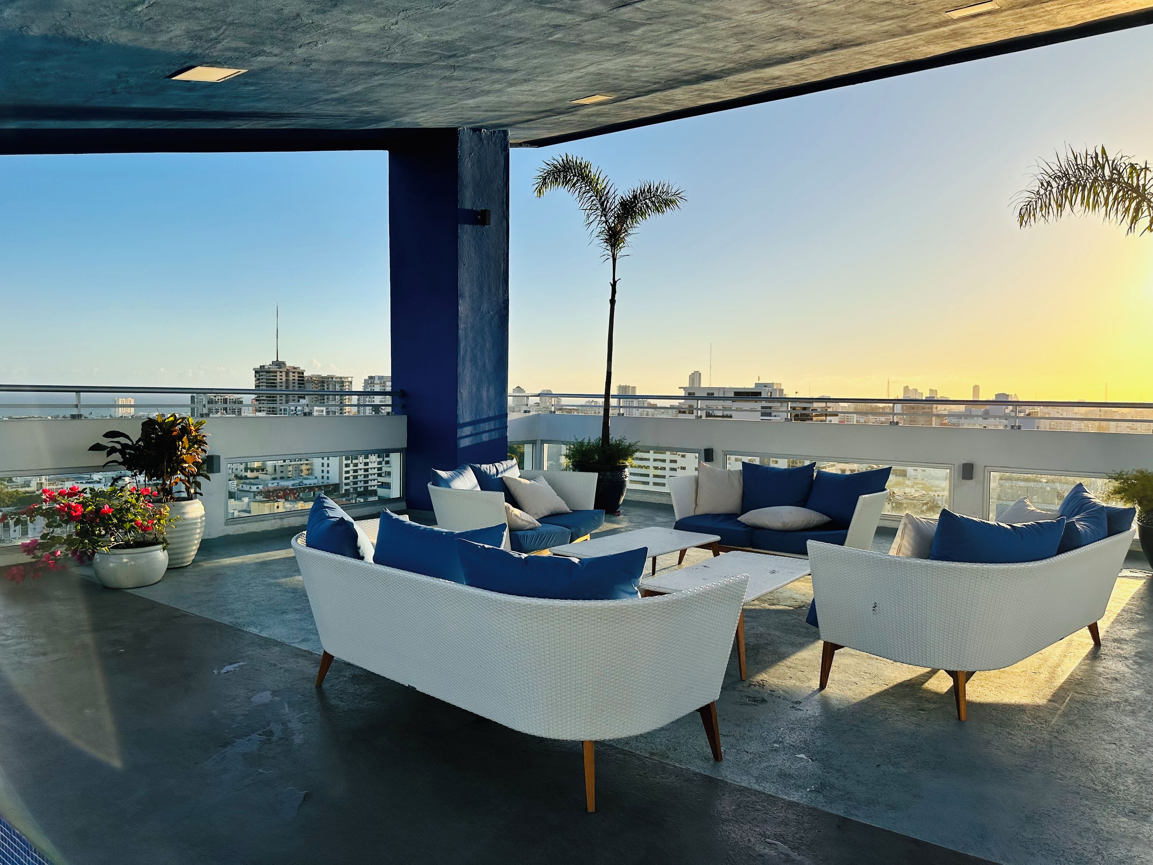 Terraza en la azotea con mobiliario exterior, plantas en macetas y vistas a la ciudad.
