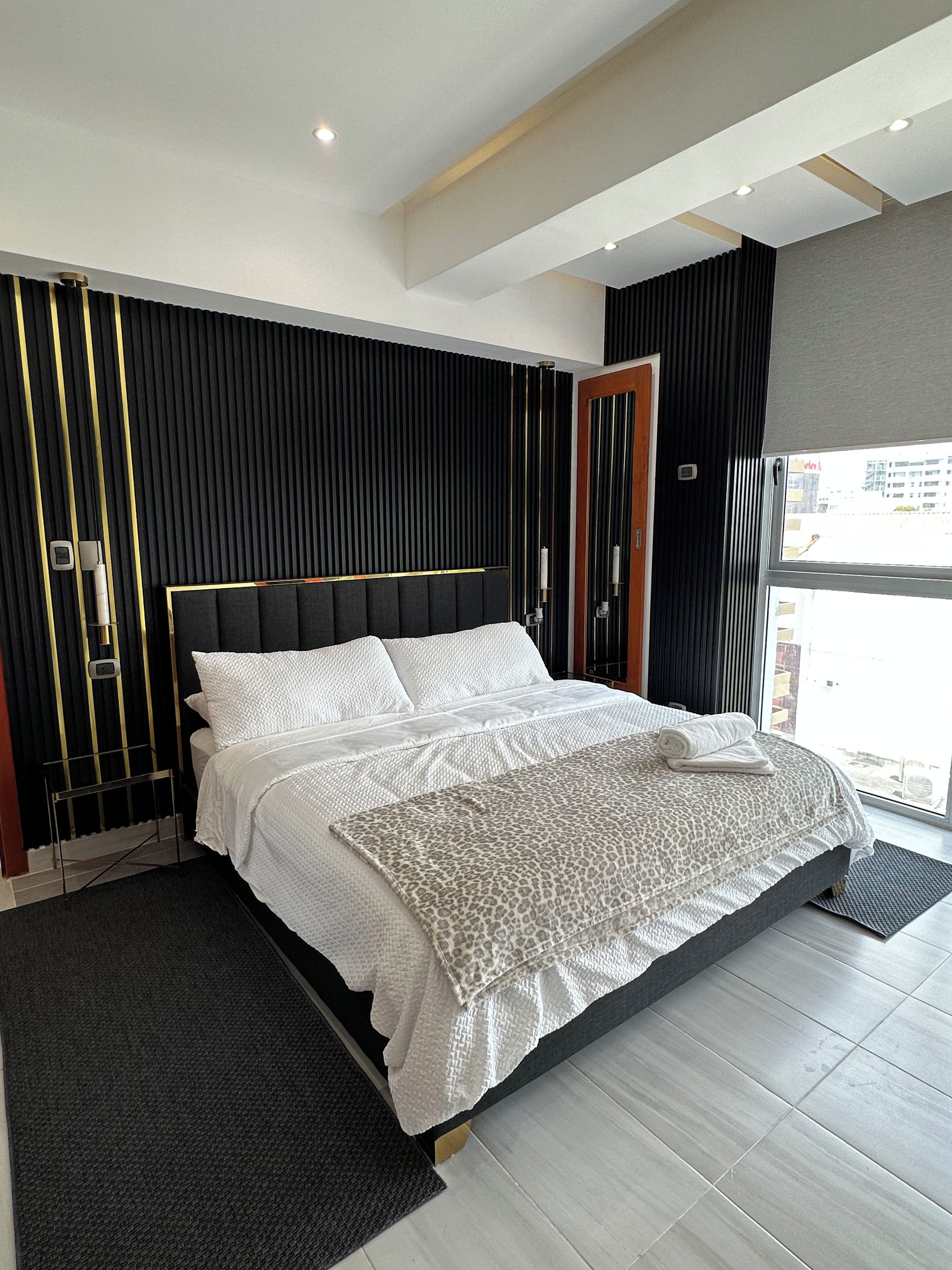 Un dormitorio moderno con una cama grande, una pared decorativa negra y dorada y vistas a la ciudad.