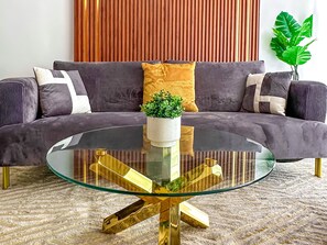 A modern living room with a glass coffee table, a dark sofa, and a potted plant. - Prime Location / Modern 2-Bedroom Apartment / 2 Bathrooms / Pool / Gym / 1 King-Size Bed (Santo Domingo)