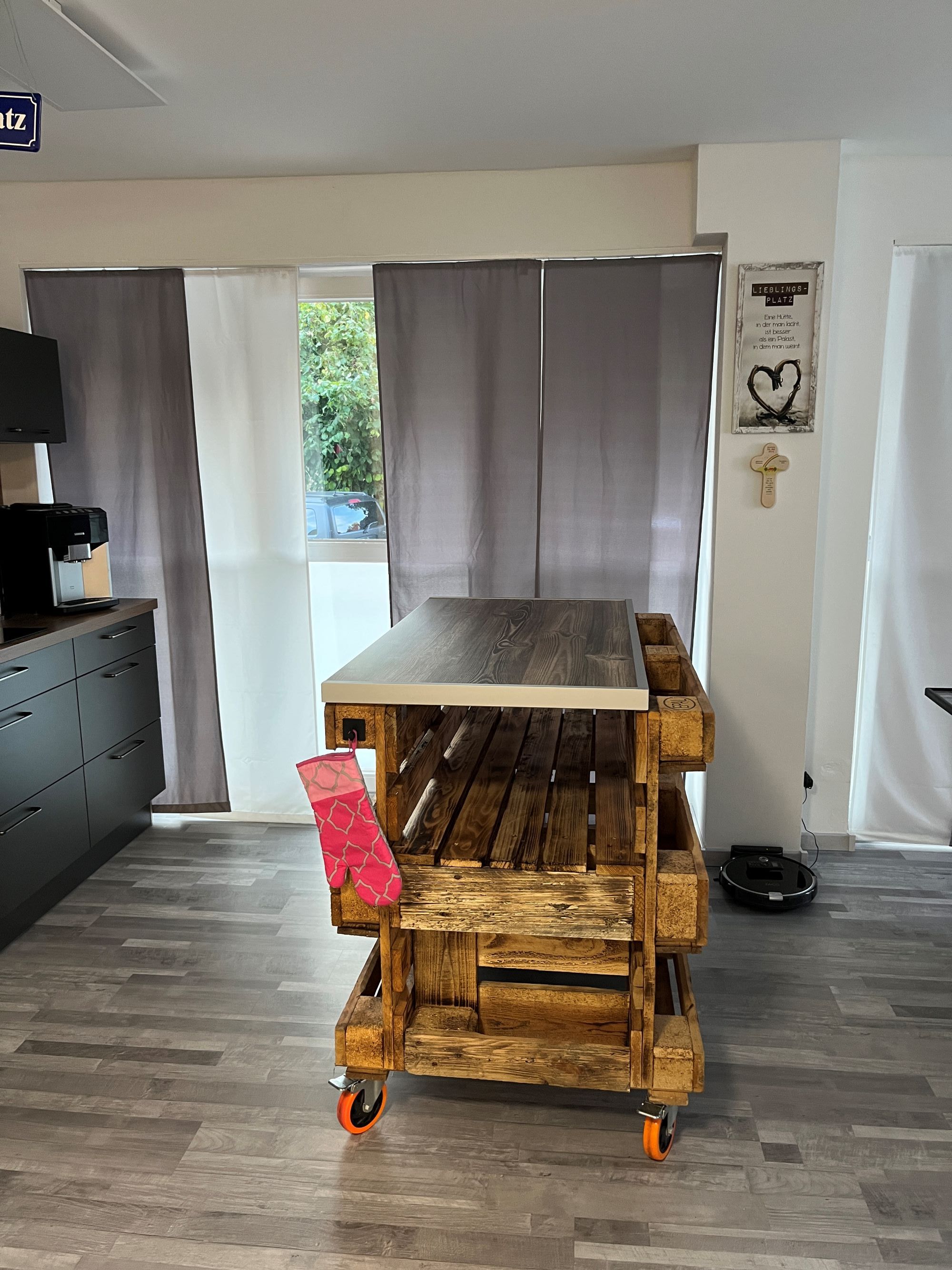 Ein Zimmer mit einem Tisch auf Rollen, einer Kaffeemaschine und Blick auf Grün.