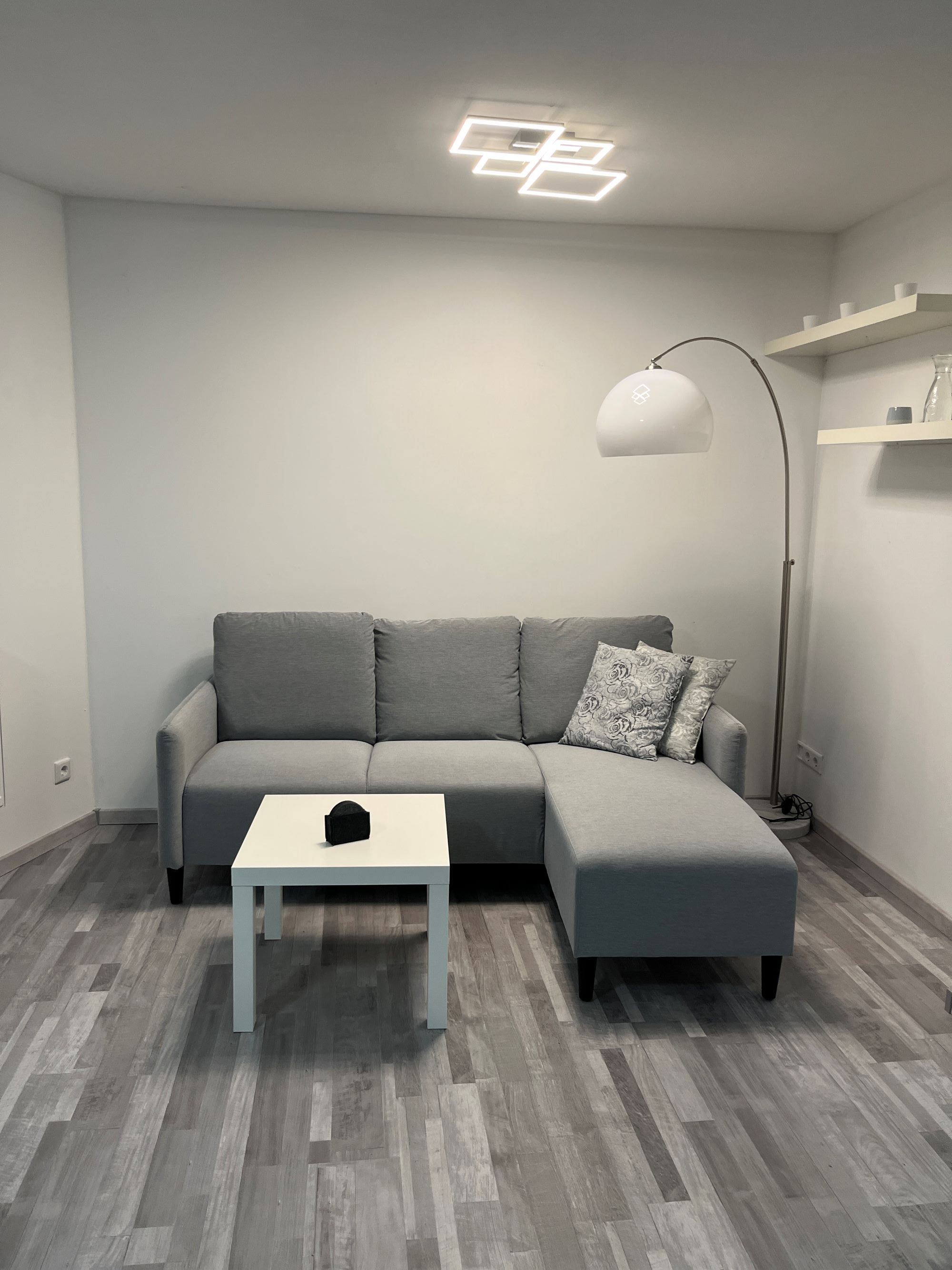 Un soggiorno moderno con un divano modulare grigio, un tavolino bianco, una lampada da terra e un cuscino decorativo.