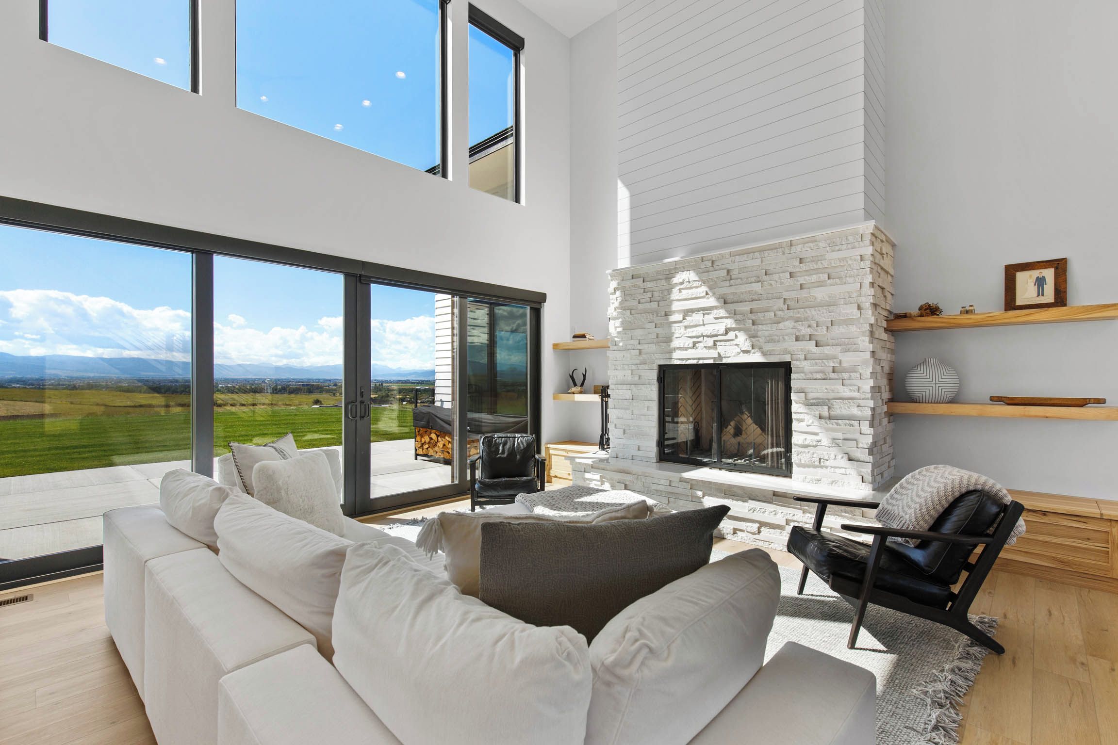 A modern living room with a white fireplace, large windows, and a view of the countryside.