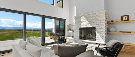 A modern living room with a white fireplace, large windows, and a view of the countryside.