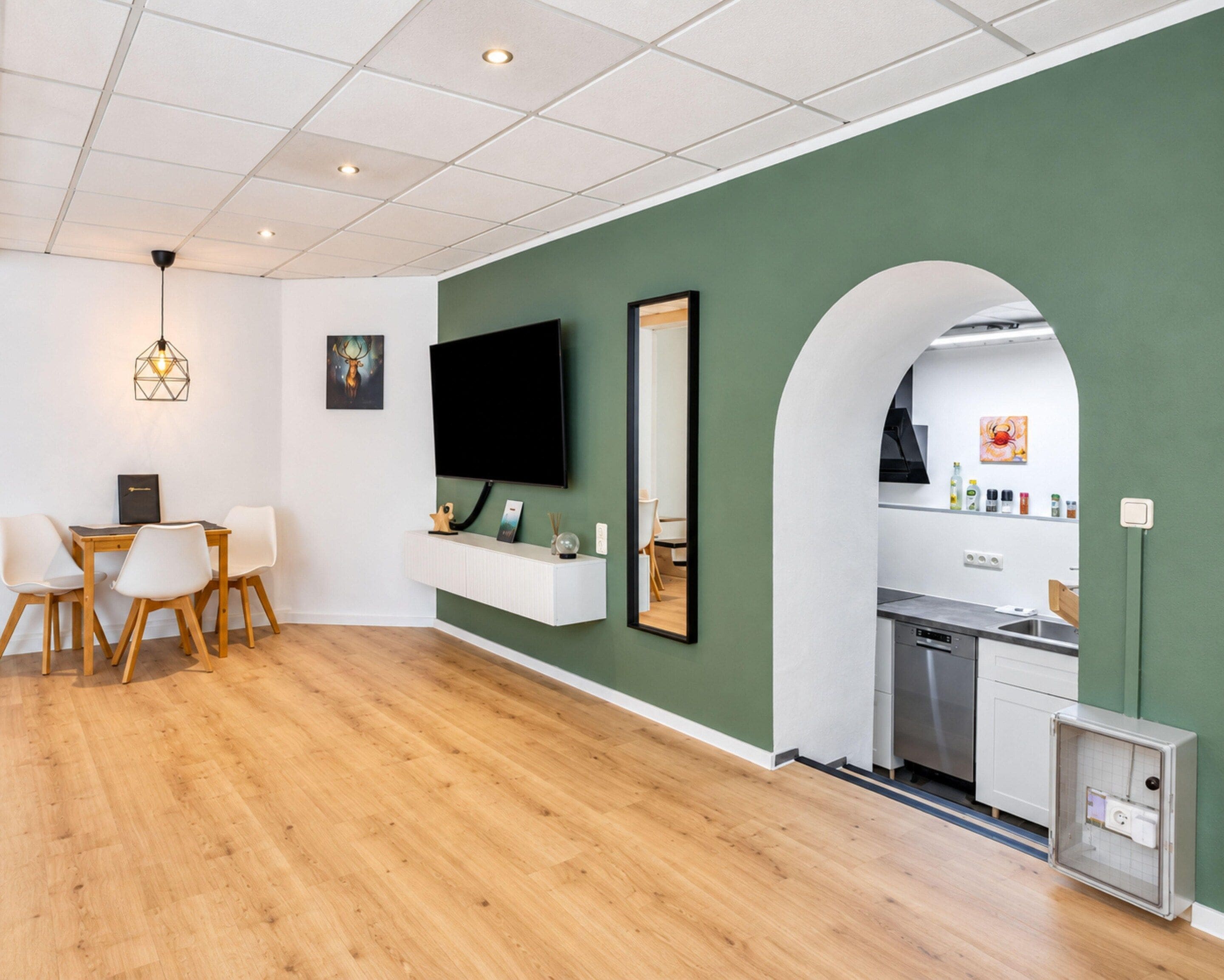 A modern living space with a dining area, kitchen, and a large mirror.