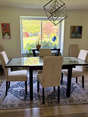 A dining area with a glass table, striped chairs, a patterned rug, and a view of a garden through a large window. - Charming pet friendly 3-bedroom house with deck and fenced yard Bloomfield (Bloomfield)