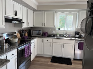 A modern kitchen with white cabinets, stainless steel appliances, a microwave, and a window with plants. - Charming pet friendly 3-bedroom house with deck and fenced yard Bloomfield (Bloomfield)