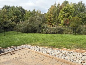 A backyard with a paved patio area, a wooden deck, and a fence. - Charming pet friendly 3-bedroom house with deck and fenced yard Bloomfield (Bloomfield)