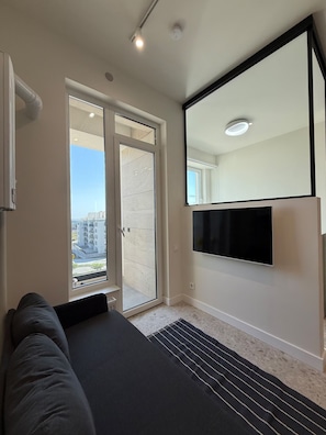 A bedroom with a bed, a TV mounted on the wall, and a sliding glass door leading to a balcony. - Cozy clean & minimalistic apartment near Airport, with balcony & view! (Chișinău)