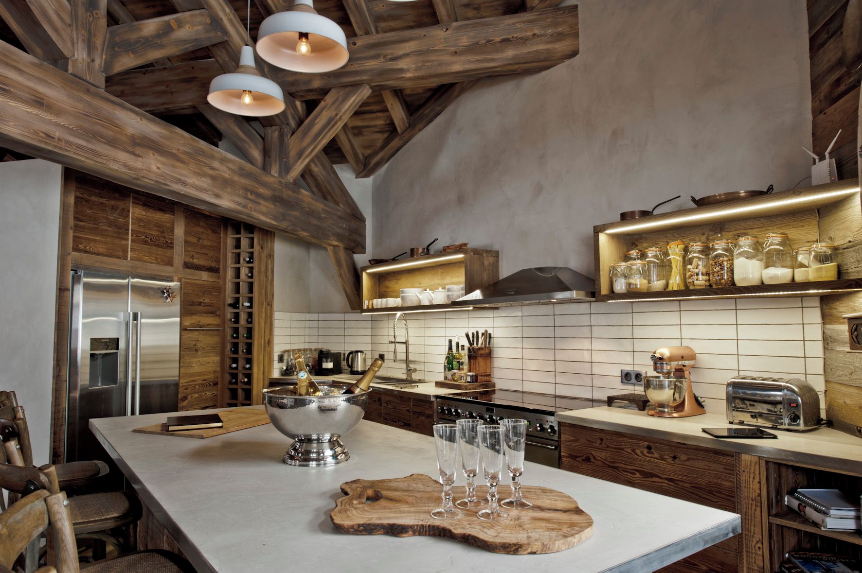 A modern kitchen with a wooden ceiling, stainless steel appliances, and a central island with glasses and bottles.