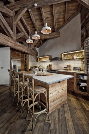 Une cuisine rustique avec des poutres en bois, un îlot central doté de tabourets et des luminaires suspendus.