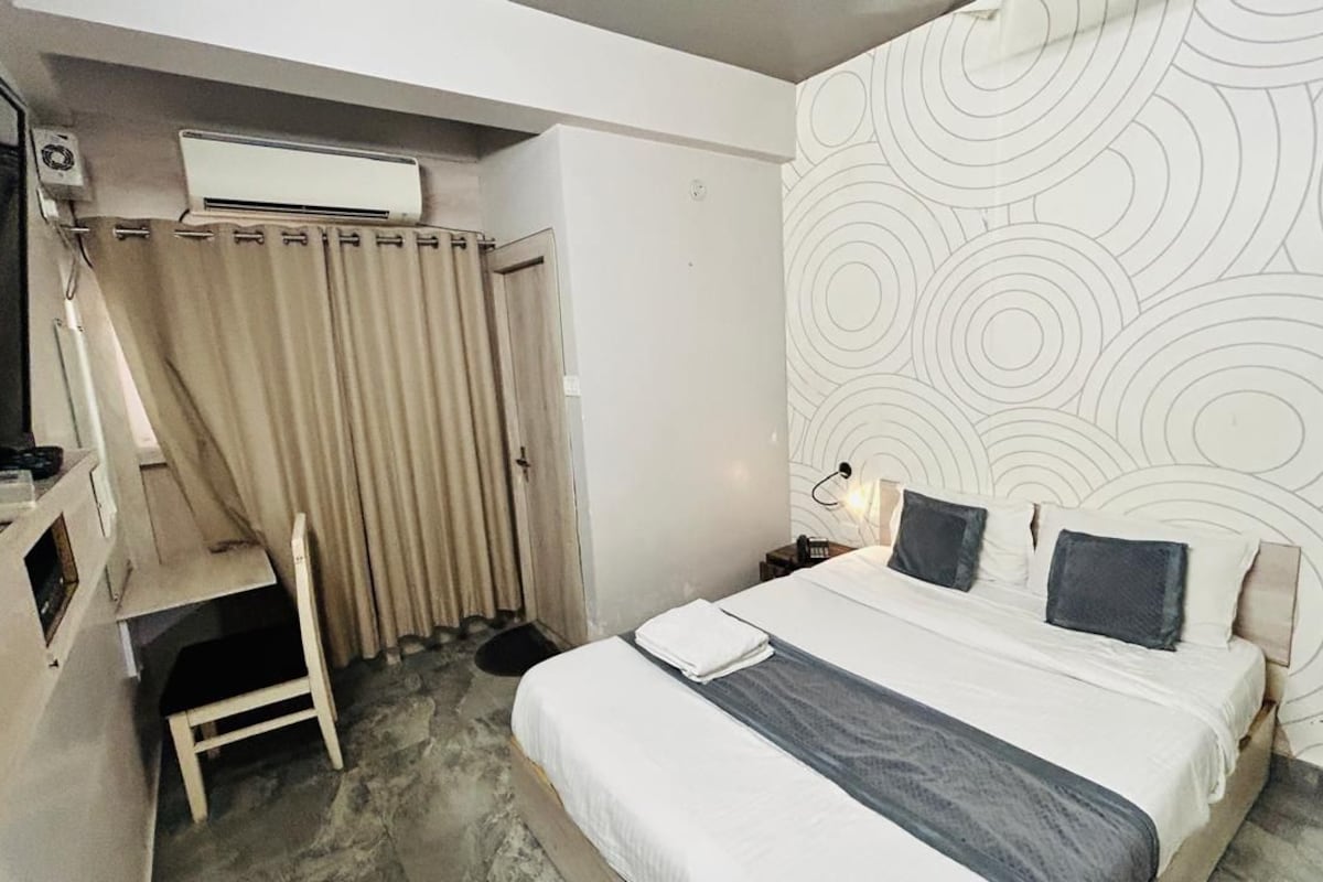 Una habitación de hotel con una cama, un escritorio, una silla, una cortina, una pared con diseño circular y un teléfono de pared.