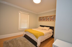 Ein Schlafzimmer mit einem Bett, einem Fenster mit Jalousien, einem Gemälde an der Wand und einem Holzboden.