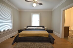 Un dormitorio con cama, mesitas de noche, ventilador de techo y ventana.