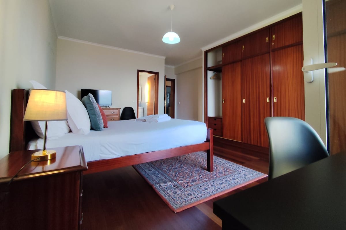 Une chambre d’hôtel comprenant un lit, une table de chevet, une lampe, une télévision, une armoire et un tapis à motifs.