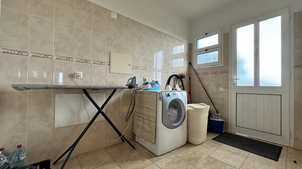 A laundry room with a washing machine, ironing board, and a small window.