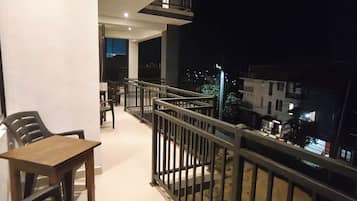 A balcony with a wooden table and chairs, a railing, and a view of the city at night.