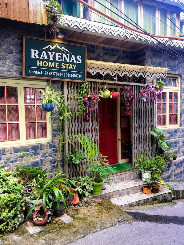 A house with a sign that reads 'RAYENAS HOME STAY' and contact numbers.
