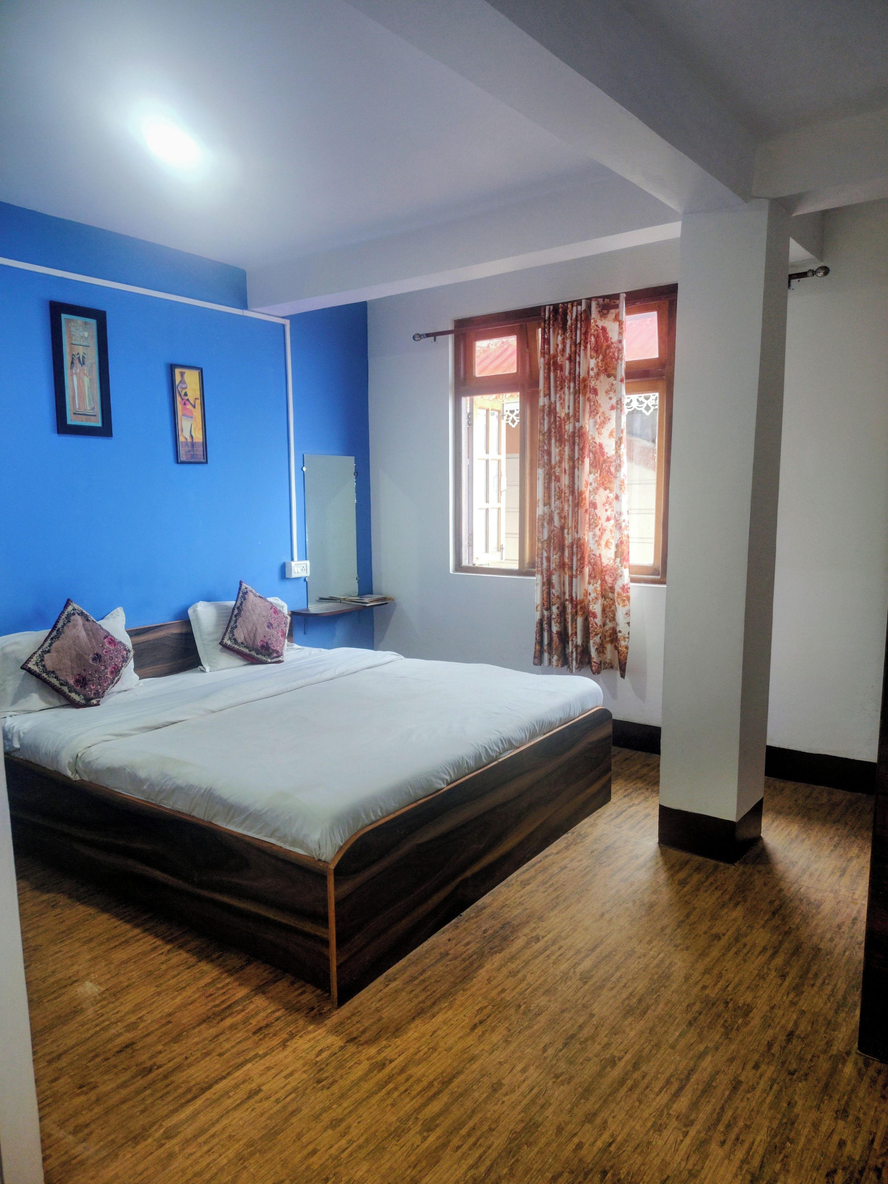 Une chambre à coucher avec un lit, une table de chevet, une fenêtre avec des rideaux et un mur bleu.