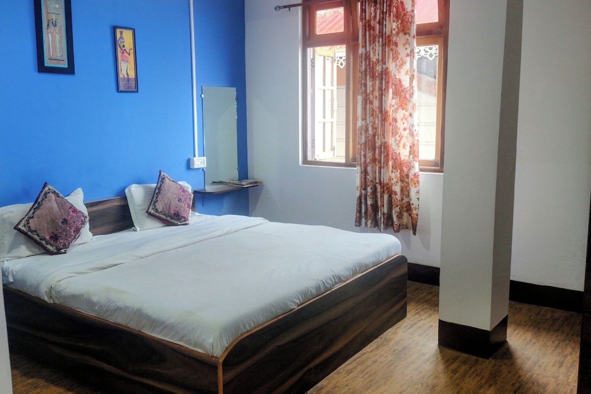 Une chambre à coucher avec un lit, une table de chevet, une fenêtre avec des rideaux et un mur bleu.
