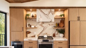 A modern kitchen with wooden cabinets, marble backsplash, and stainless steel appliances. - Luxury Chalet - Incredible 180 Views - Heated Pool (Sevierville)