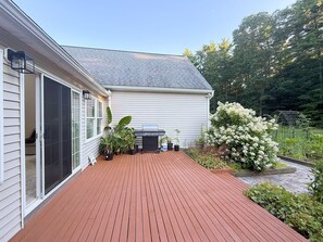 A covered deck with a grill, potted plants, and a white house with a grey roof. - Shirley Mansion - Family Stay, 3BR/2.5BA One-Level, Office, Sunroom, Yard (Shirley)