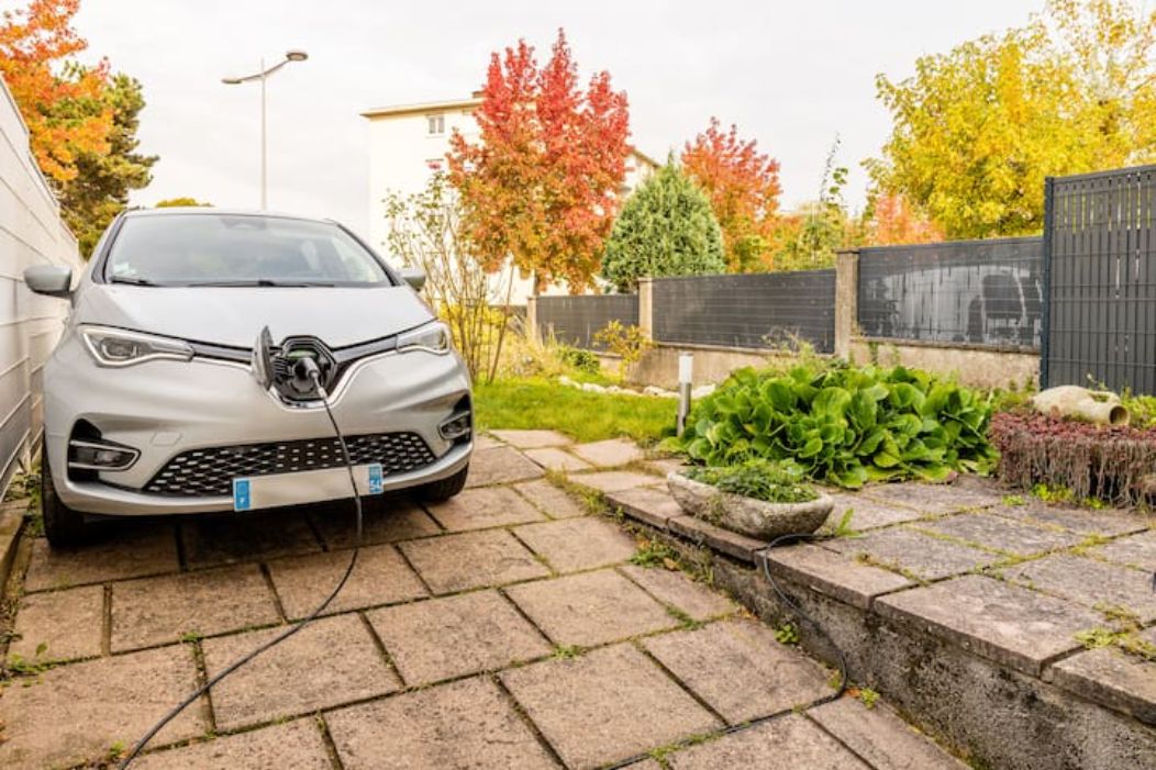 A silver car parked in a driveway with a charging station.