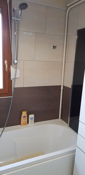 A bathroom with a bathtub, a showerhead, and two bottles of shampoo. - Vrbo Property (Vandœuvre-lès-Nancy)
