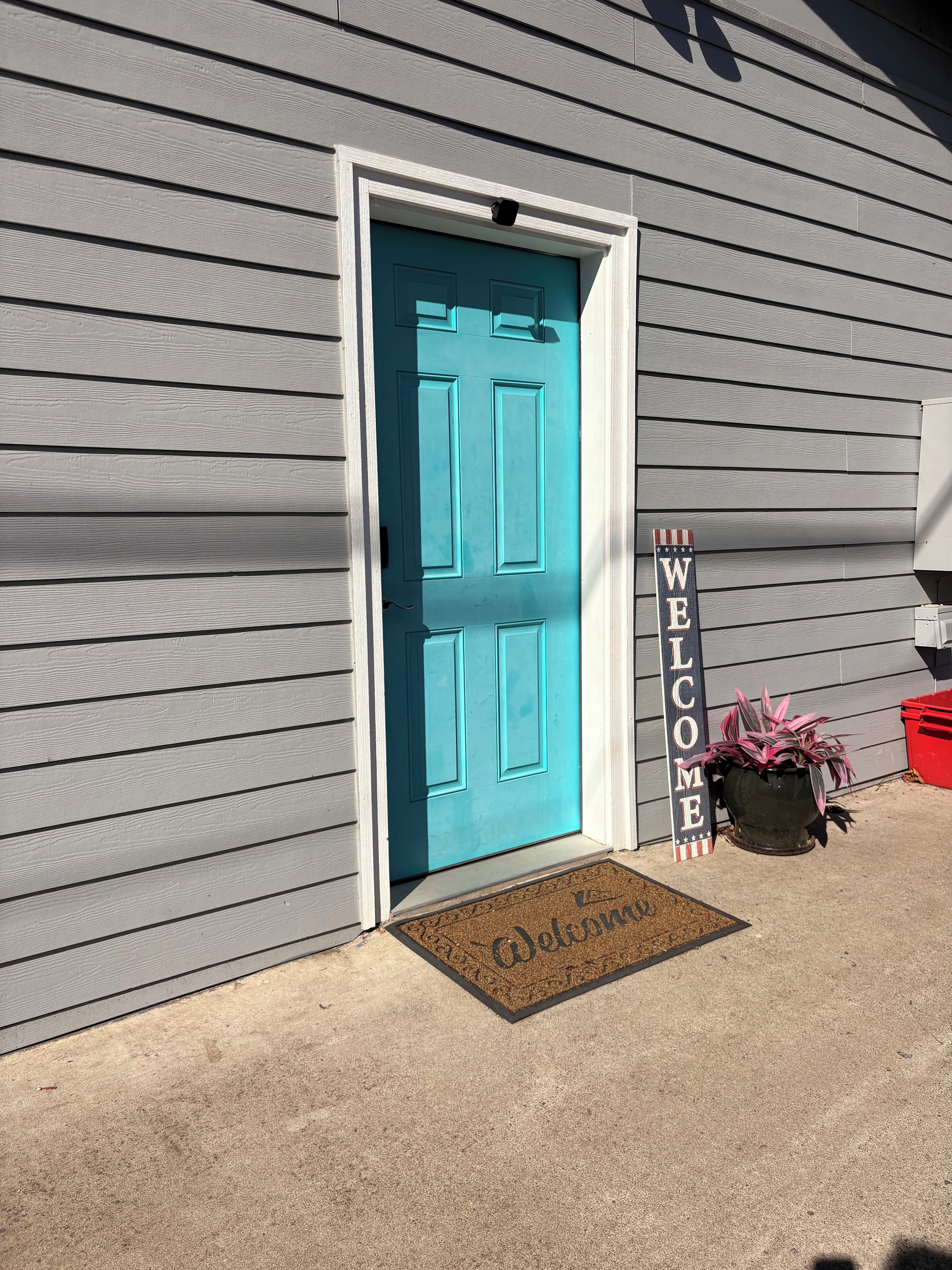 A house with a turquoise door, a welcome sign, and a doormat.