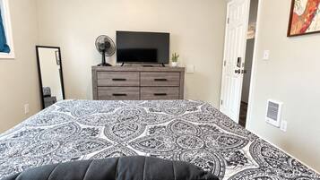 A bedroom with a bed, a dresser, a television, and a door.