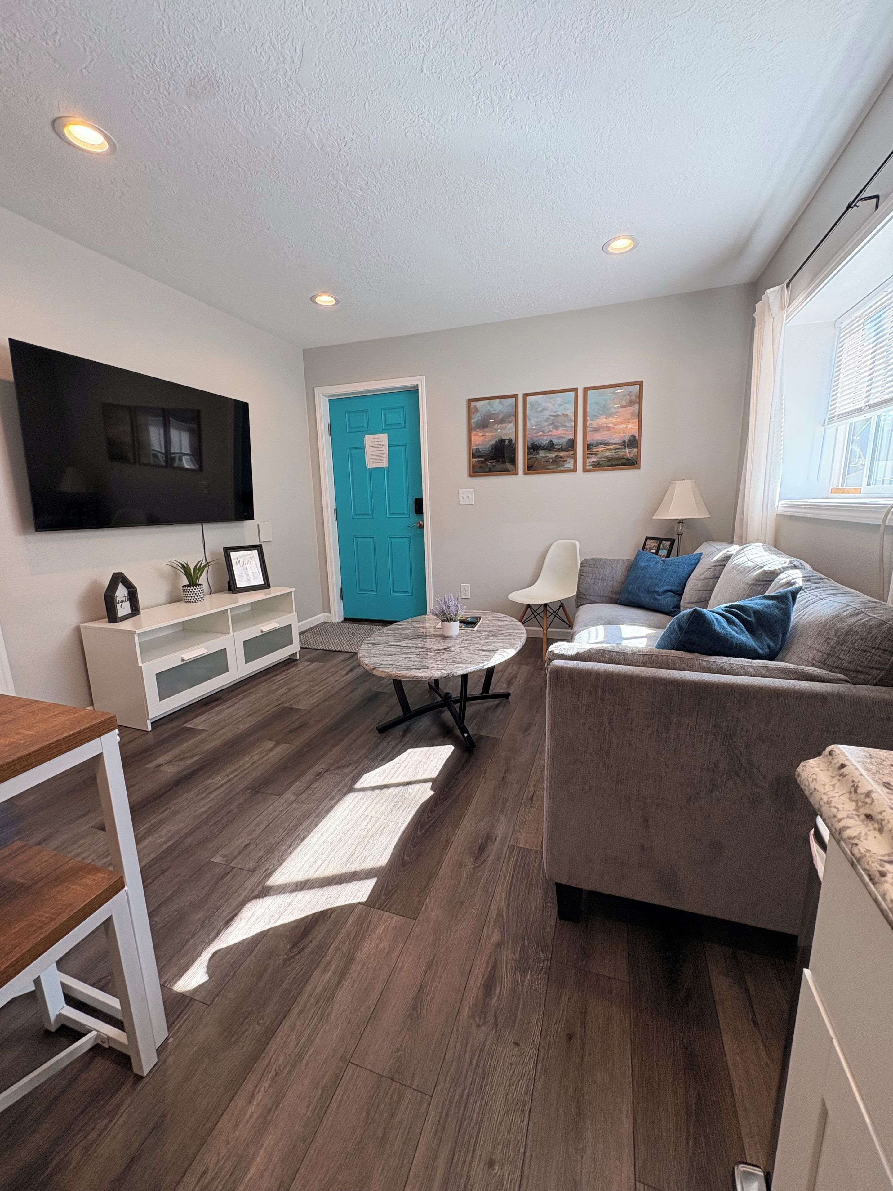 A modern living room with a flat-screen TV, a blue door, and a sofa with cushions.