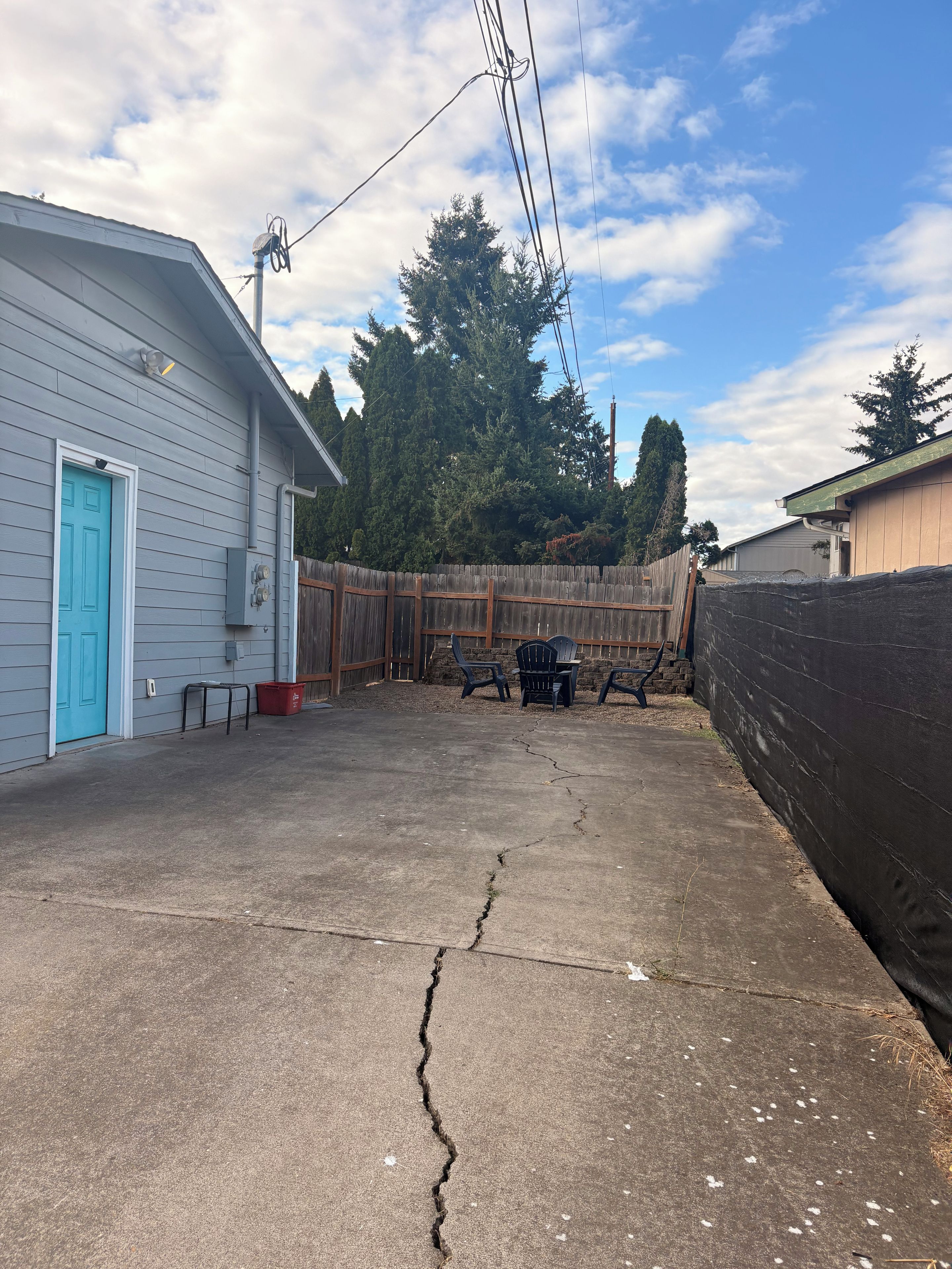 A residential backyard with a concrete patio, a wooden fence, and a blue door.