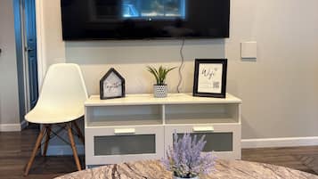 A living room with a flat-screen TV mounted on the wall, a white chair, a marble coffee table, and a small potted plant.