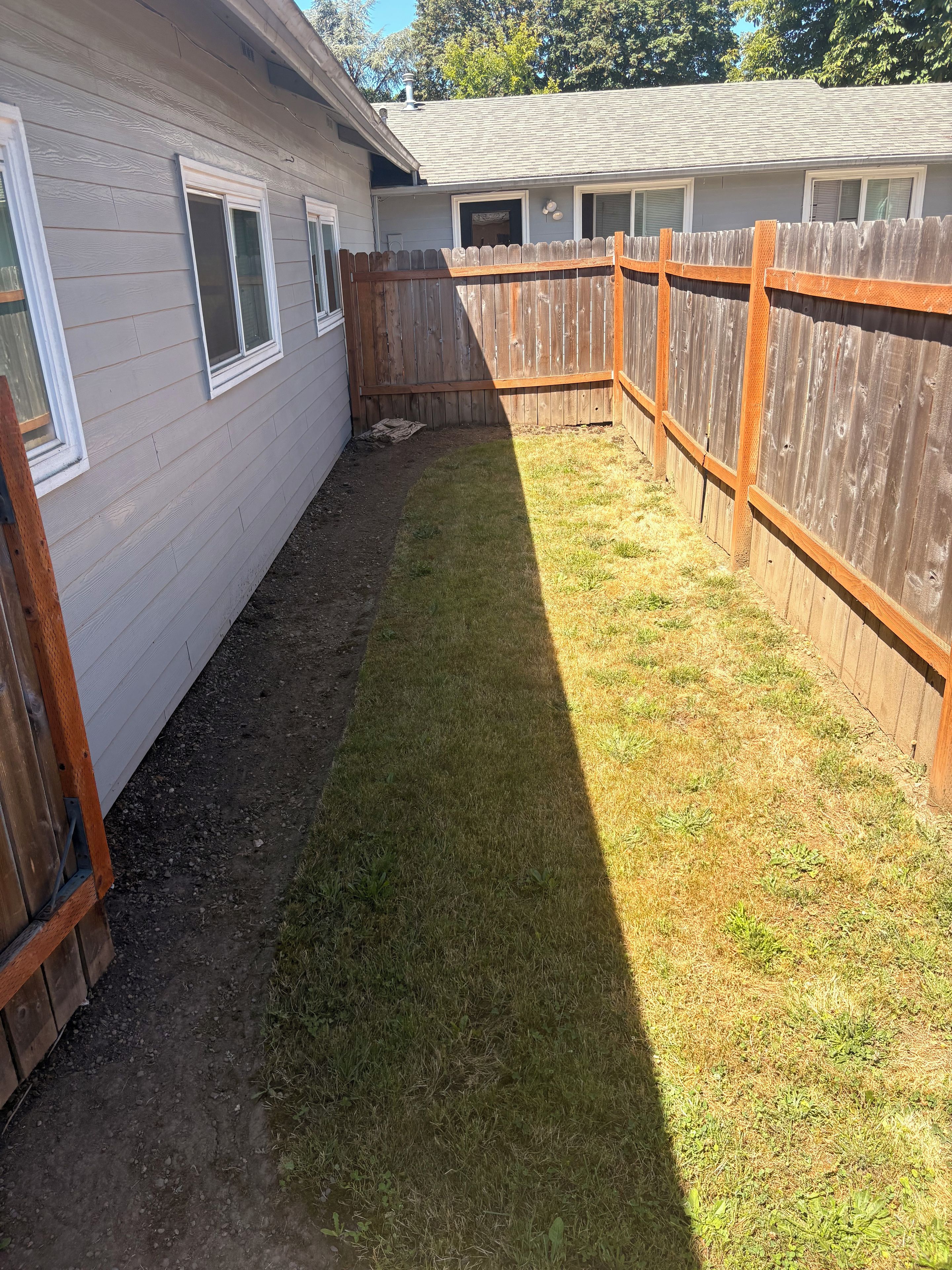 Patio trasero cercado con césped y una terraza de madera.