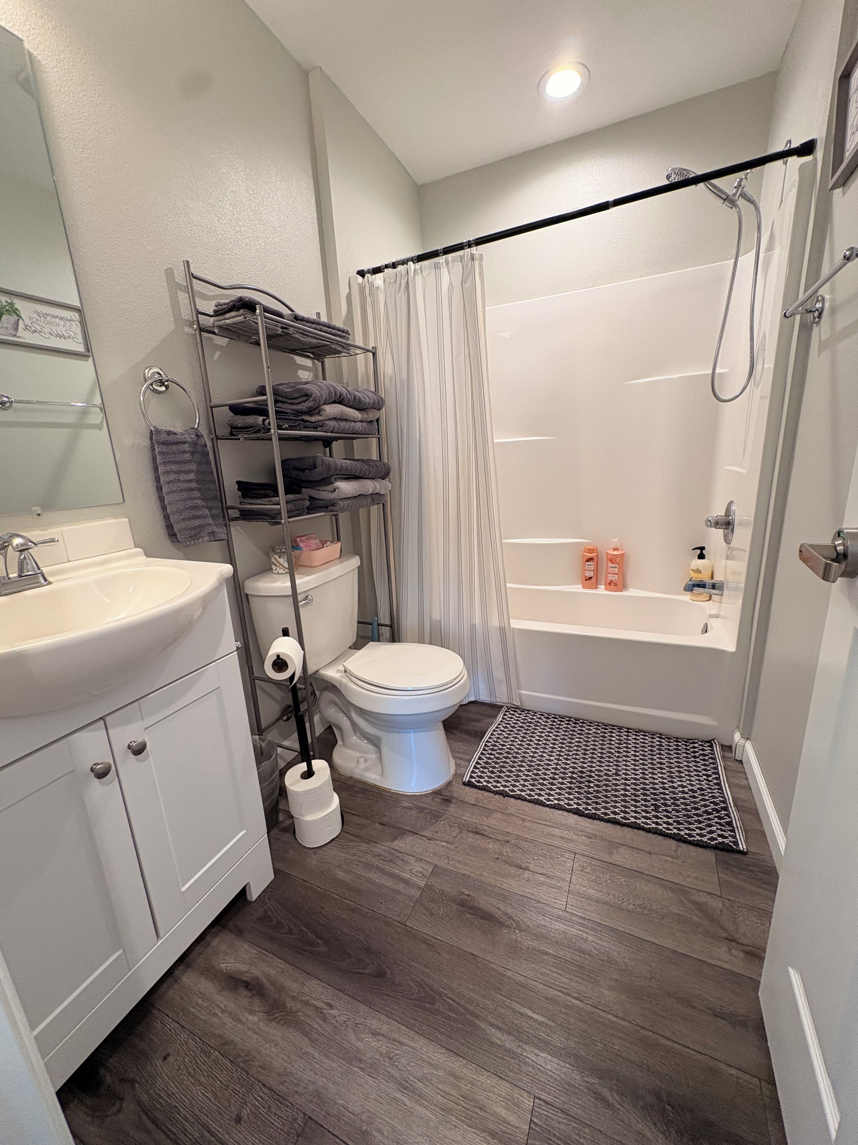 A bathroom with a toilet, sink, shower, and a towel rack with folded towels.
