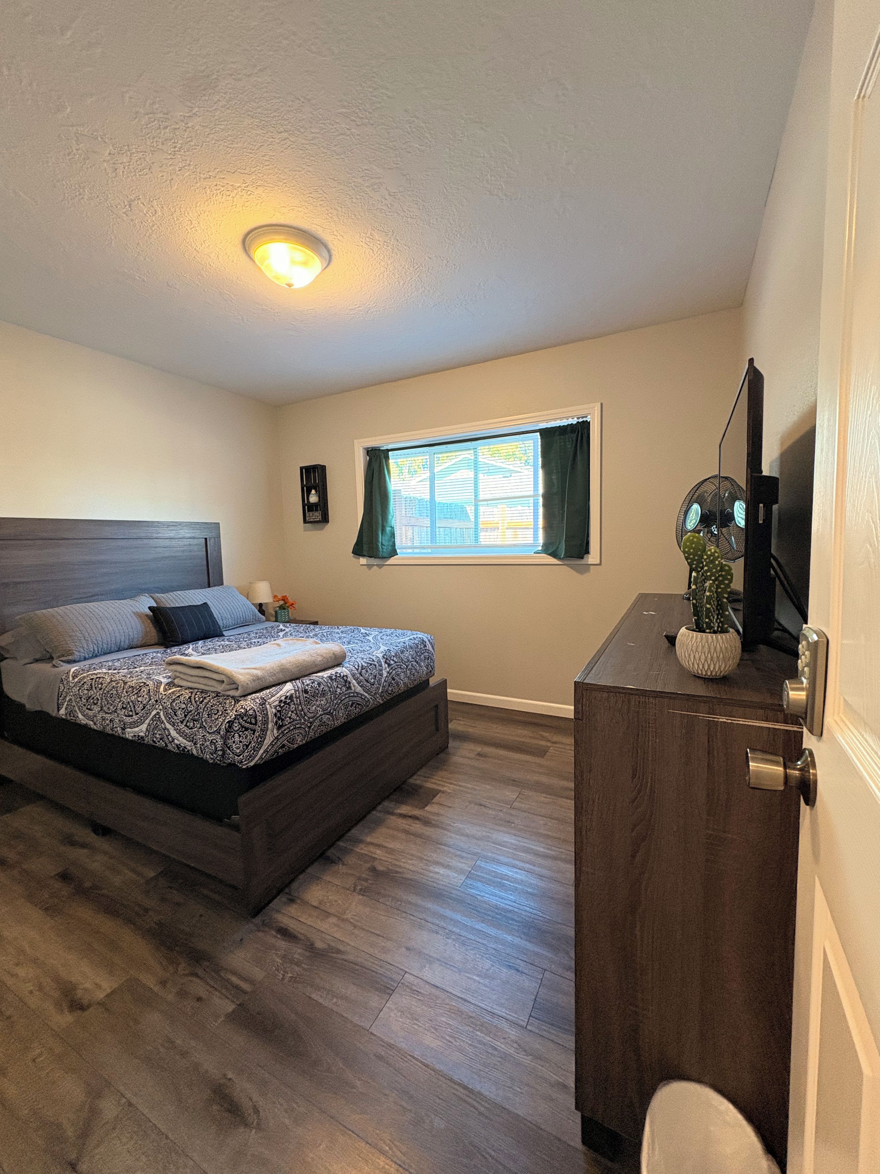 A bedroom with a bed, a desk, a window, and a ceiling light.
