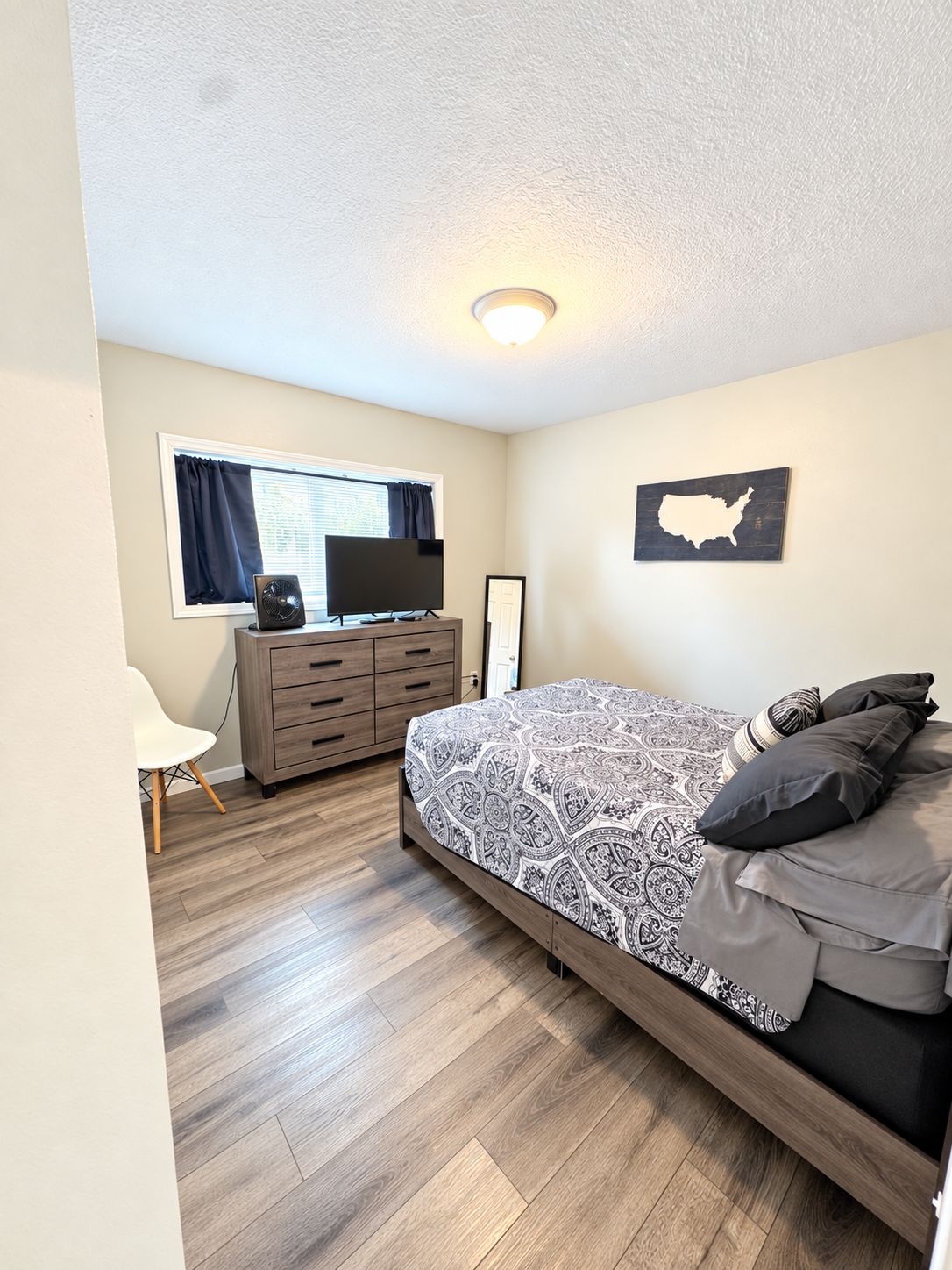 A bedroom with a bed, a dresser, a television, and a wall map.