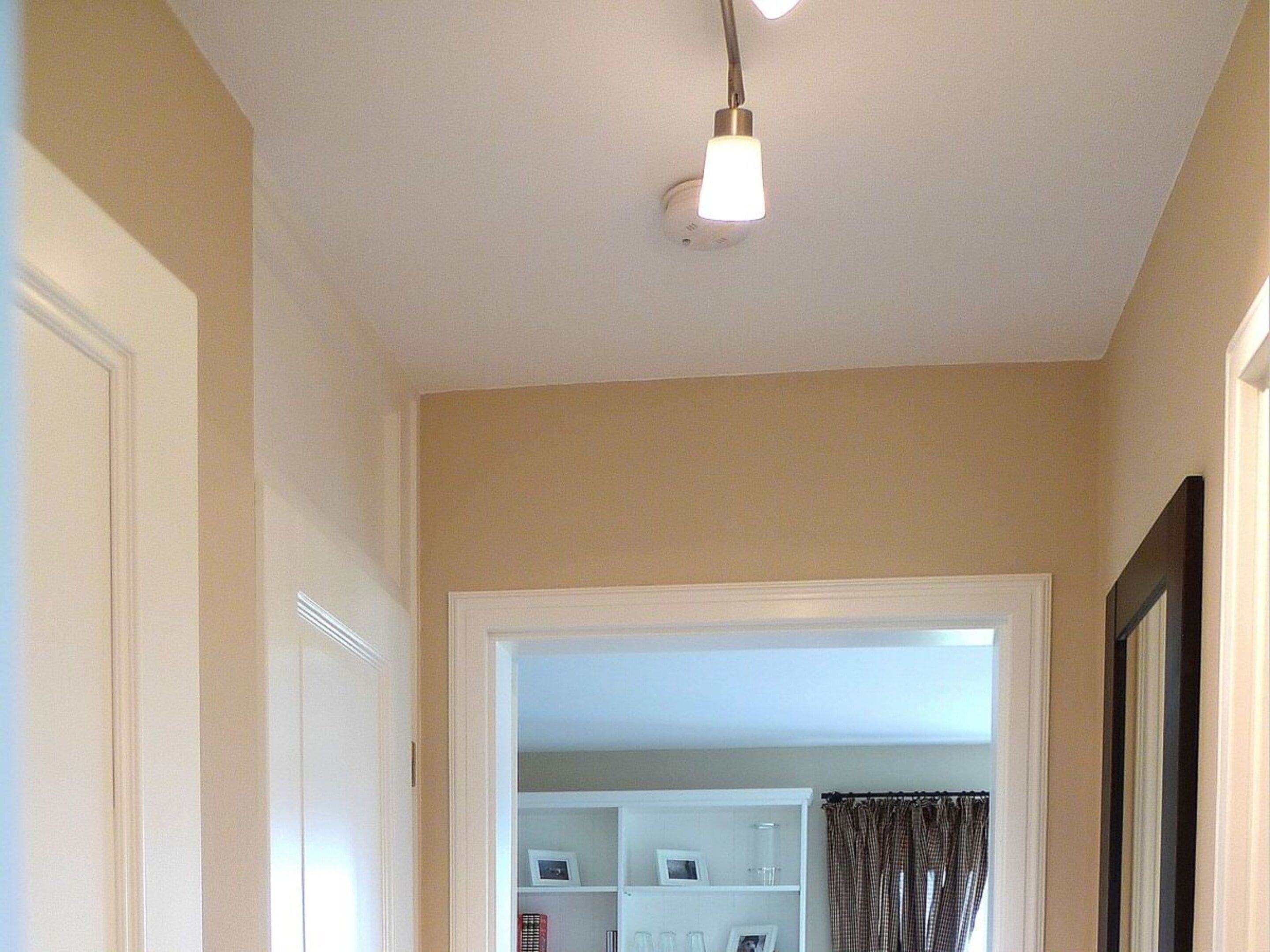 A hallway with a ceiling light fixture, a door on the left, and a view into a room with a closet and curtains.