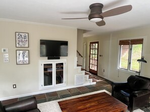 A living room with a television, a ceiling fan, a staircase, and a view of the outdoors. - Mountain Glow Hideaway (Blowing Rock)