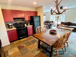 A kitchen with red cabinets, a black stove, and a dining table with chairs. - Mountain Glow Hideaway (Blowing Rock)