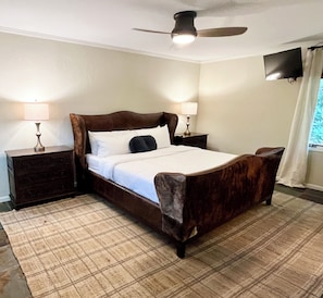 A bedroom with a wooden bed, two bedside tables, a ceiling fan, and a TV mounted on the wall. - Mountain Glow Hideaway (Blowing Rock)