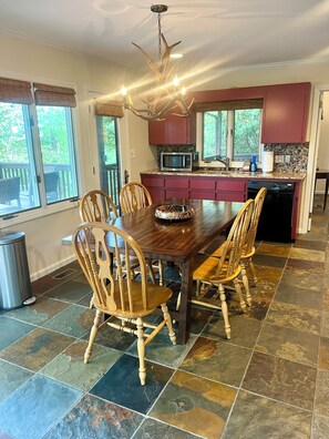A dining area with a wooden table and chairs, a chandelier, and a kitchen with red cabinets and a microwave. - Mountain Glow Hideaway (Blowing Rock)