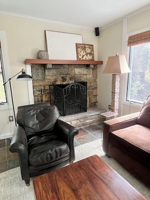 A living room with a stone fireplace, a black leather armchair, a wooden coffee table, and a brown sofa. - Mountain Glow Hideaway (Blowing Rock)
