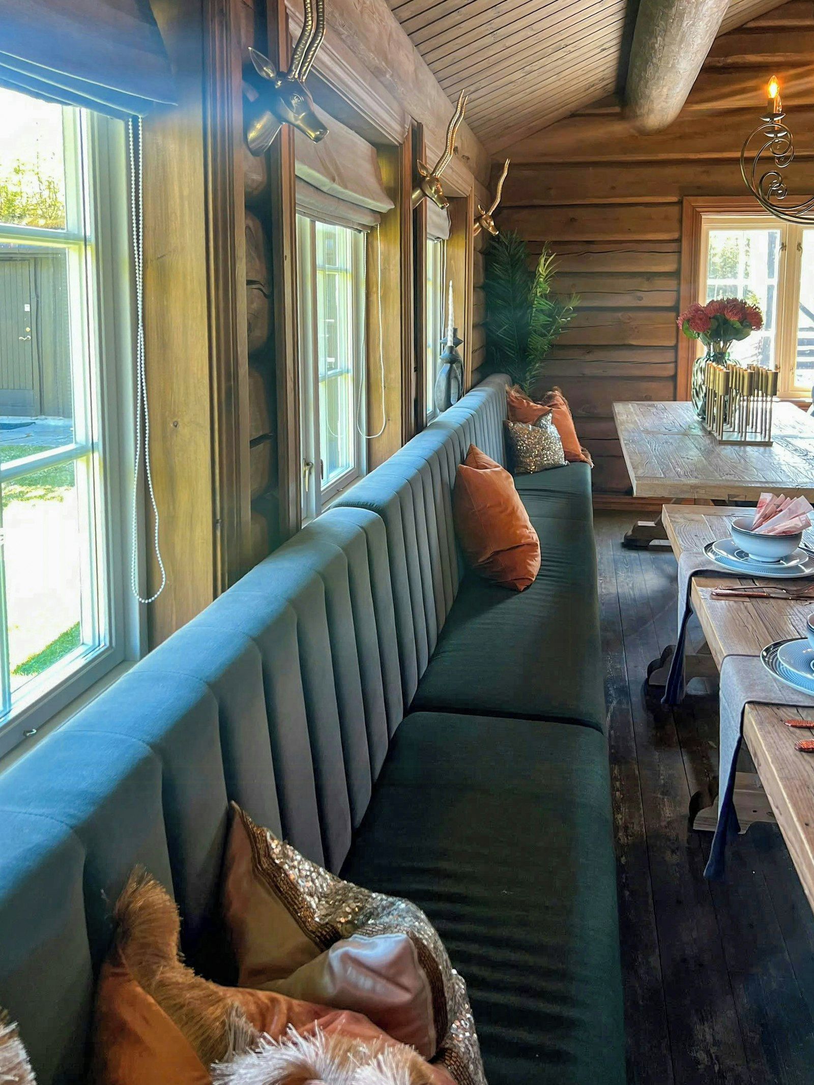 A long, cushioned bench with decorative pillows, a wooden table with a vase of flowers, and a chandelier.