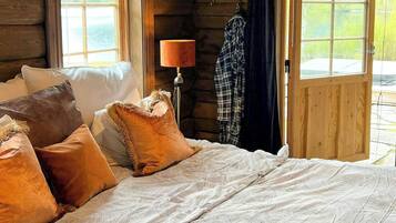 A log cabin bedroom with a bed, pillows, a lamp, and a view of the outdoors.