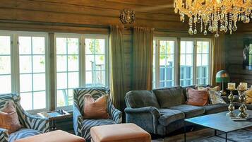 A spacious living room with a large chandelier, leather sofas, ottomans, and a coffee table.